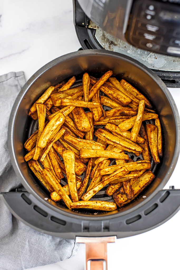 Air fryer basket filled with roasted parsnips.