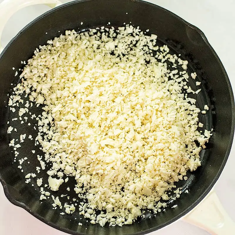 raw cauliflower rice in a cast iron skillet.