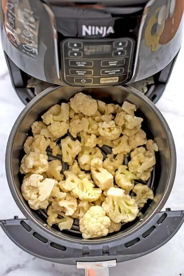 Frozen cauliflower in air fryer basket before cooking