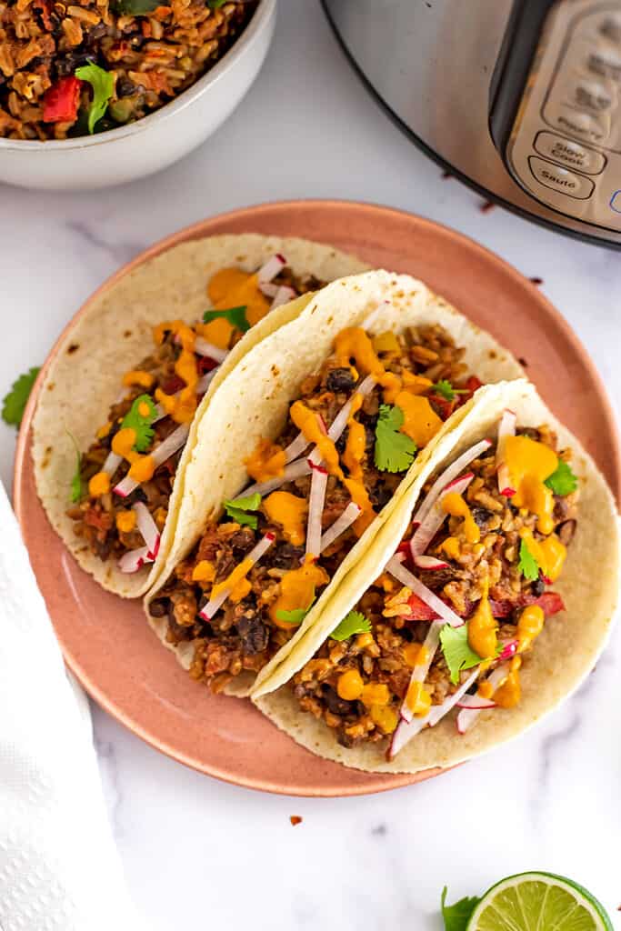 Three tacos filled with Mexican rice and beans on pink plate.