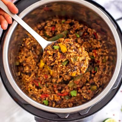 Instant pot filled with Mexican rice and beans, silver spoon taking a scoop.