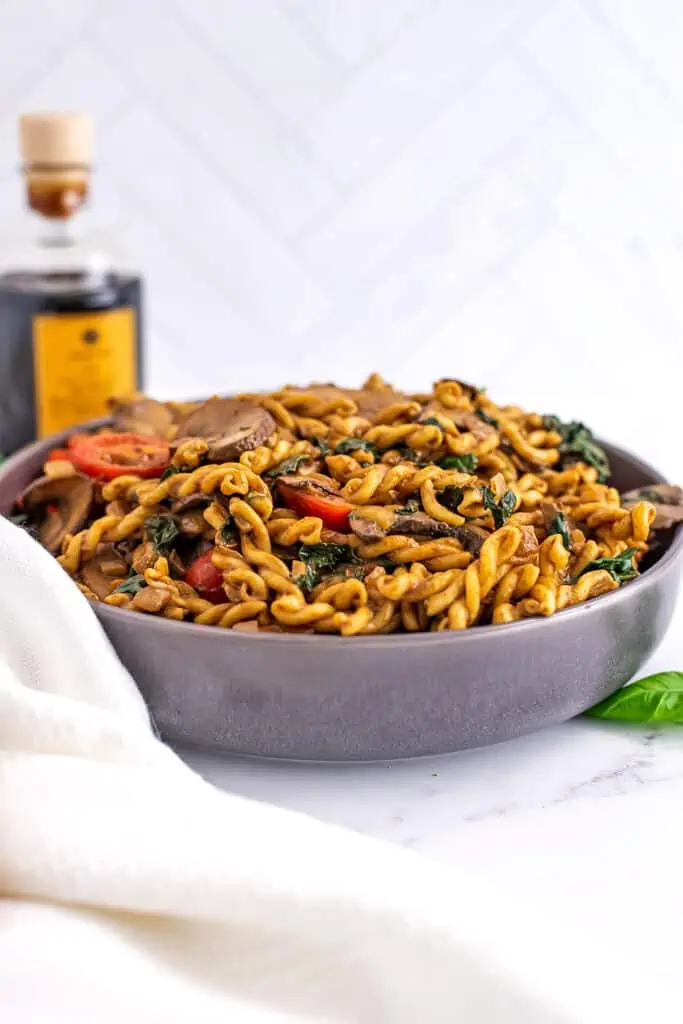 Grey bowl filled with kale mushroom pasta, balsamic vinegar in background.