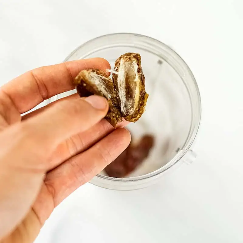 Hand holding a pitted date over a blender cup.