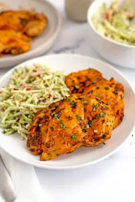 Buffalo chicken on a white plate with ranch broccoli slaw.