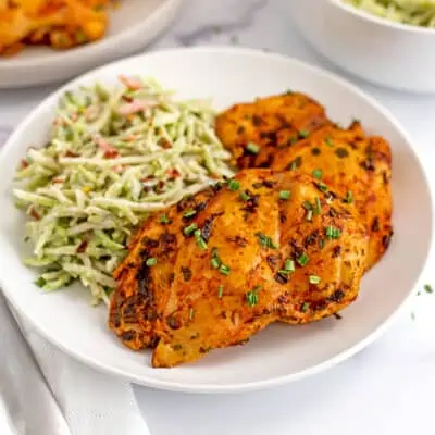 Buffalo chicken thighs on a white plate with ranch broccoli slaw.