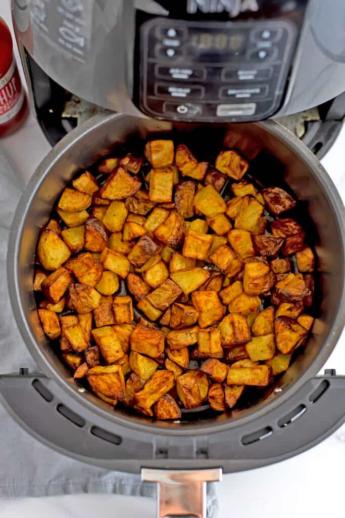 Golden brown potato cubes in an air fryer basket.
