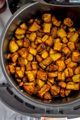 Cubed potatoes in air fryer basket after cooking.