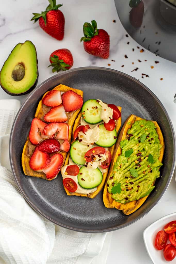 Sweet potato toast on grey plate with three different toppings, strawberries, veggies and hummus, avocado.