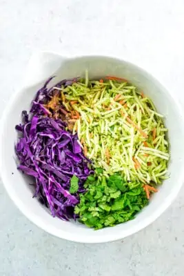 Broccoli slaw, cilantro and red cabbage in large white bowl.