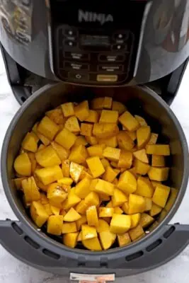 Diced potatoes in air fryer basket before cooking.