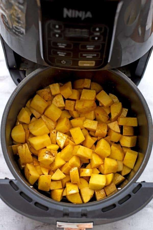 Diced potatoes in air fryer basket before cooking.