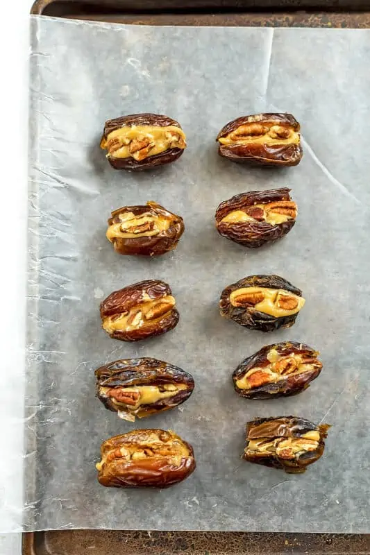 Dates on baking sheet with peanut butter and pecans stuffed inside. 