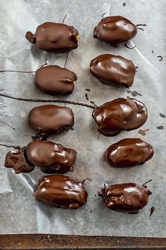 Dates covered in melted chocolate on baking sheet.