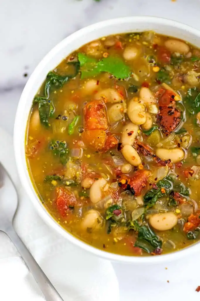 Large bowl filled with spicy white bean stew with spoon on the side.
