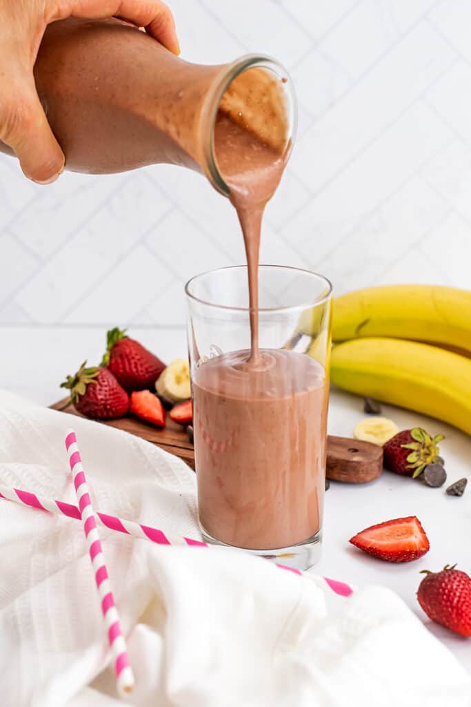 Strawberry banana chocolate smoothie being poured into a glass.