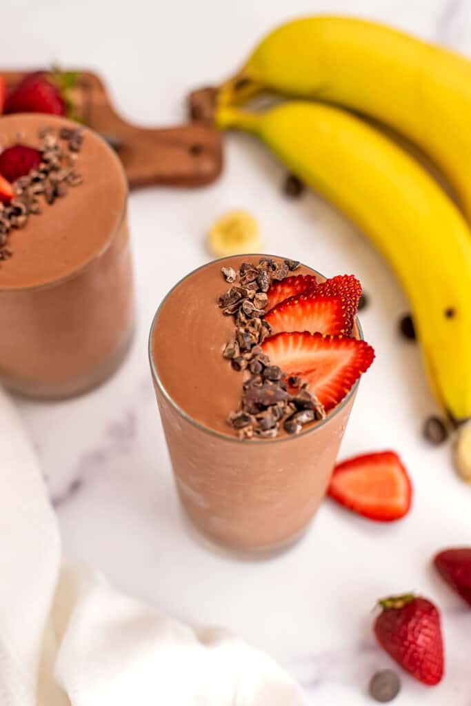Cacao nibs and sliced strawberries on top of a glass filled with strawberry banana chocolate smoothie.