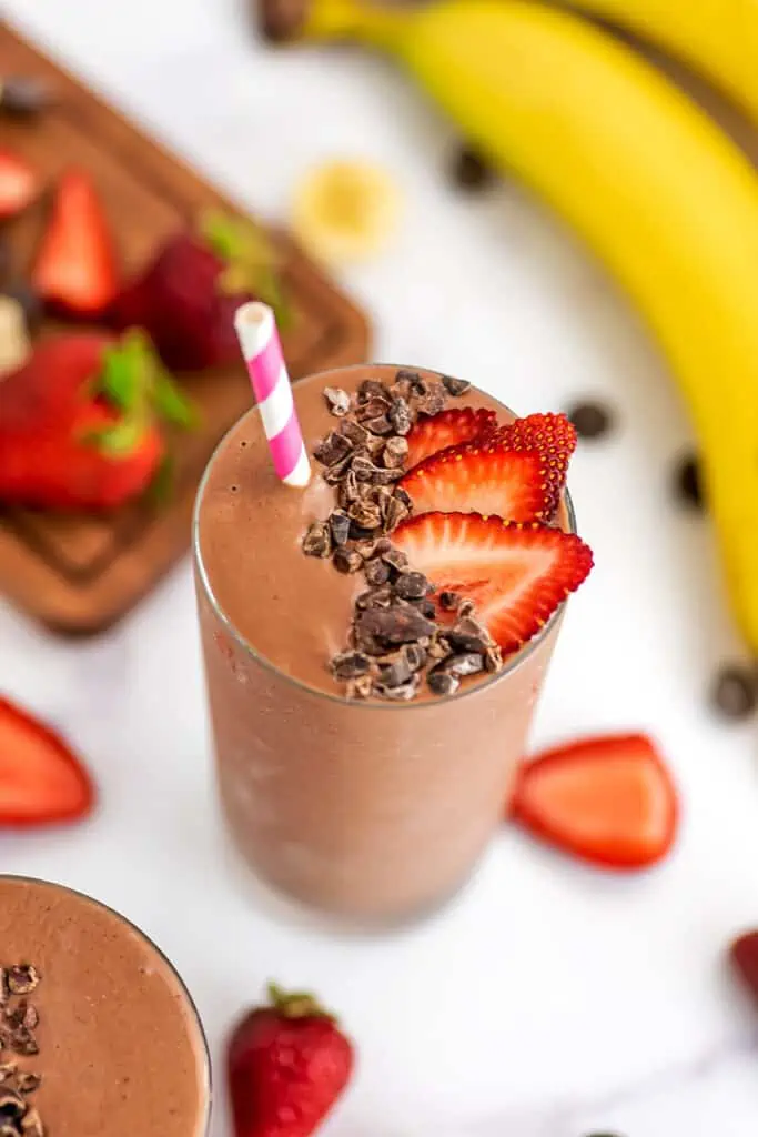 Strawberry banana chocolate smoothie in a glass with sliced strawberries and bananas in background.