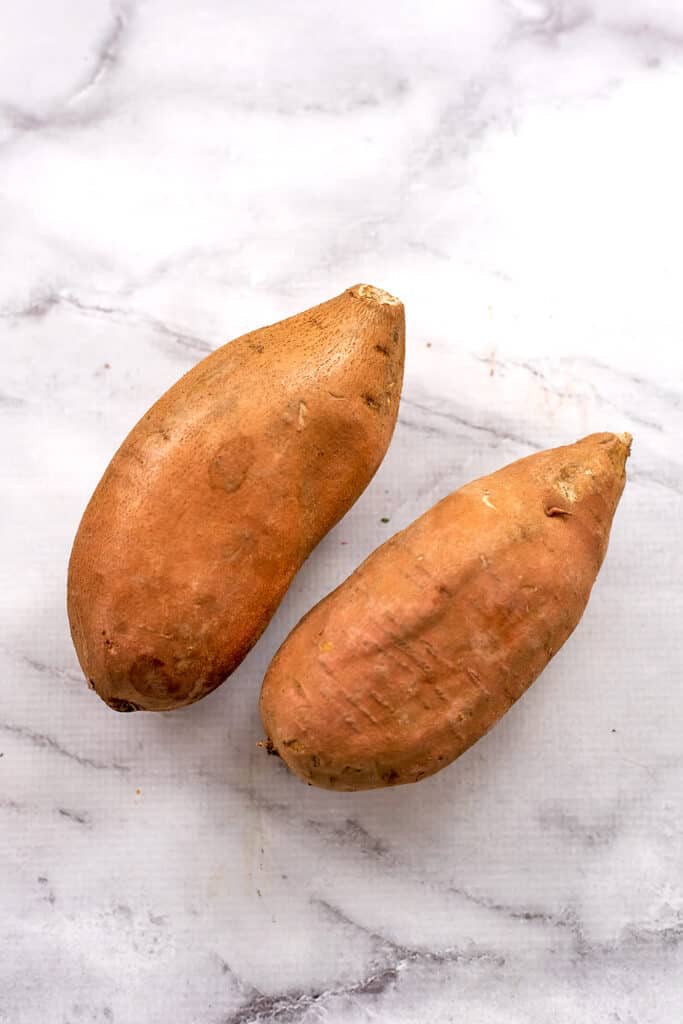 Two large sweet potatoes on a marble countertop.
