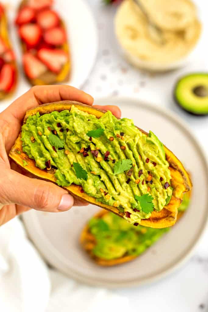 Hand holding sweet potato toast with avocado smashed on top.