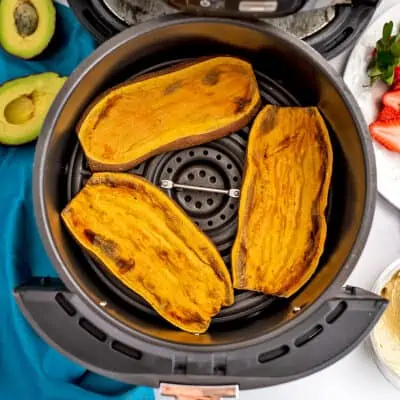 Sweet potato toast in air fryer basket, avocado in background.