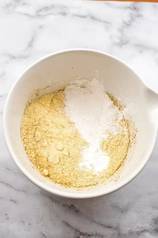 Almond flour blackberry muffins dry ingredients being added to wet ingredients in large white bowl.