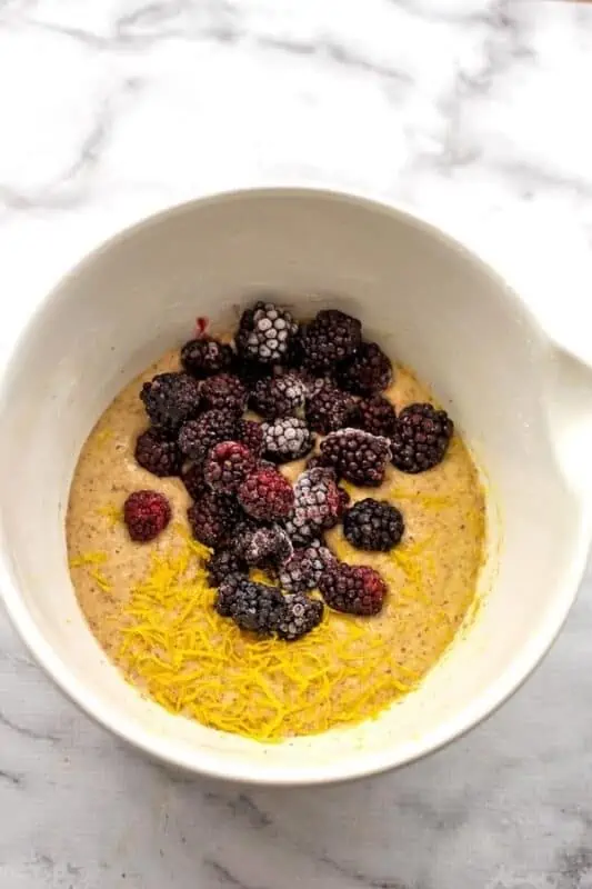 Frozen blackberries and lemon zest added to bowl of almond flour blackberry muffins.