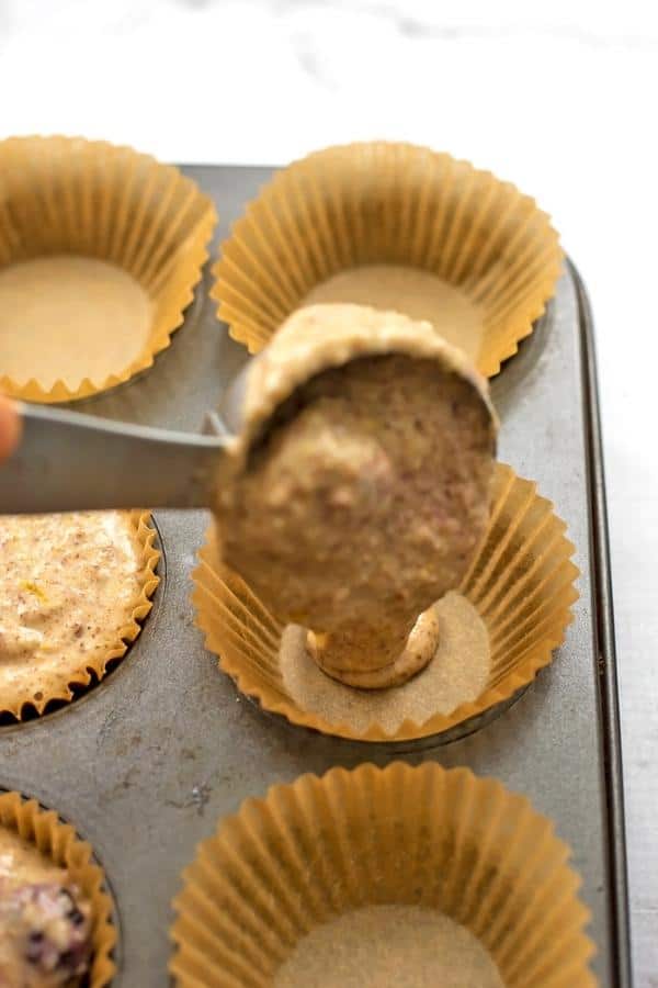 Measuring cup scooping batter into muffin tin.