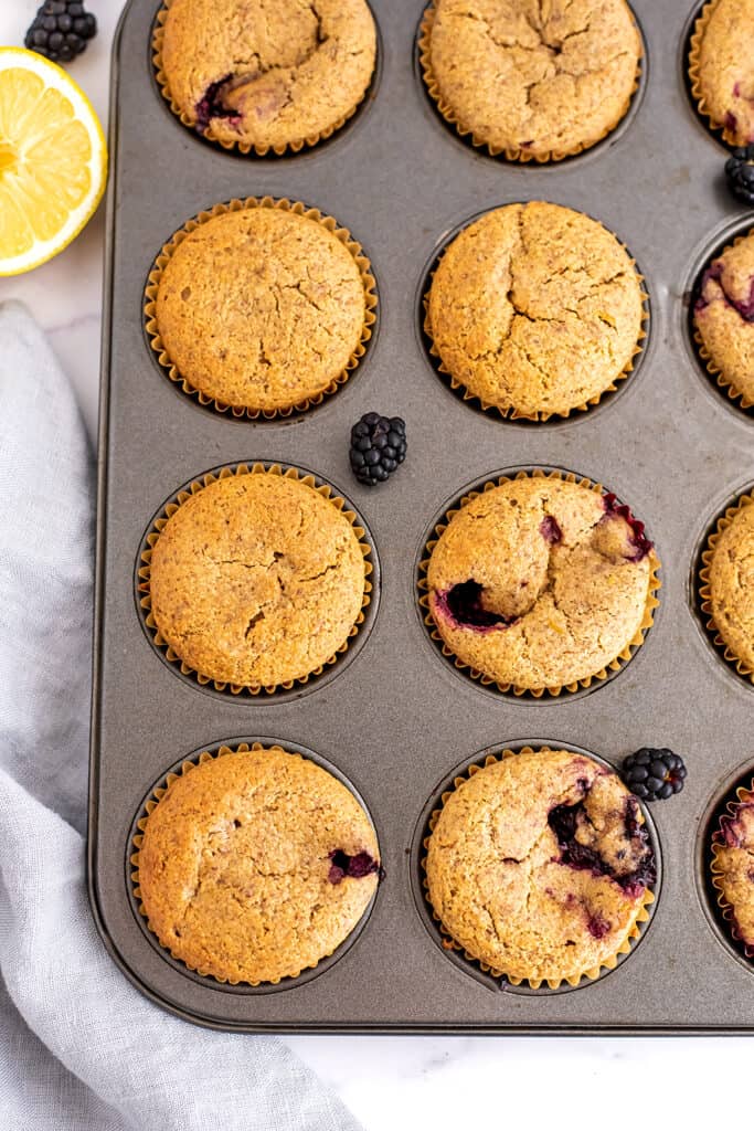 Almond flour blackberry muffins in a muffin tin with a napkin on the side.