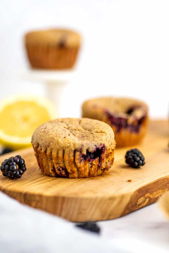 Two vegan blackberry muffins on a wooden tray with lemon in background.