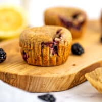 Vegan blackberry muffins on a wooden tray with blackberries around the muffins.