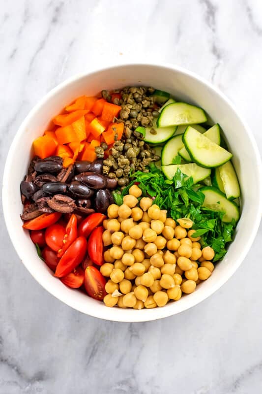 Large bowl filled with chickpeas, chopped veggies, olives and capers. 