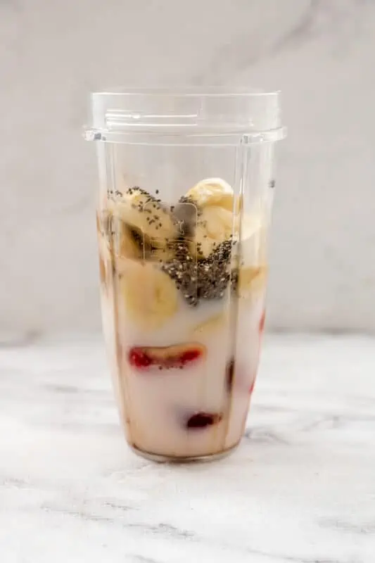 Ingredients to make strawberry banana chocolate smoothie in blender cup.