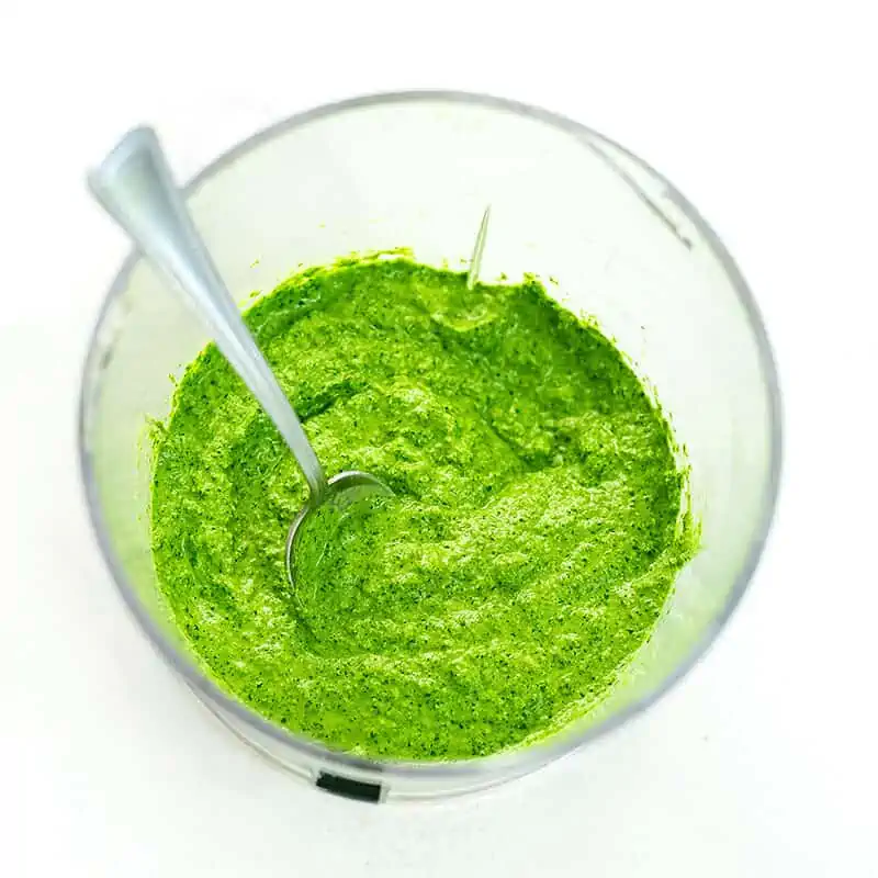 Spoon resting in food processor full of spinach walnut pesto.