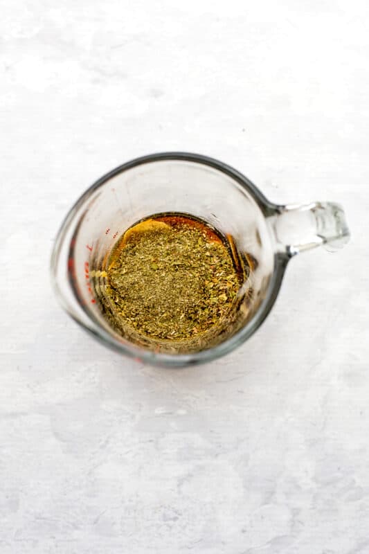 ingredients to make greek marinade in glass measuring cup.