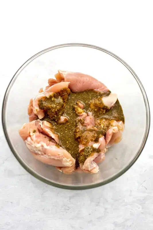 chicken thigs in a glass bowl with greek marinade.