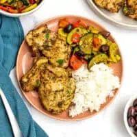 Air fryer Greek chicken on a pink plate with rice and Greek veggies.
