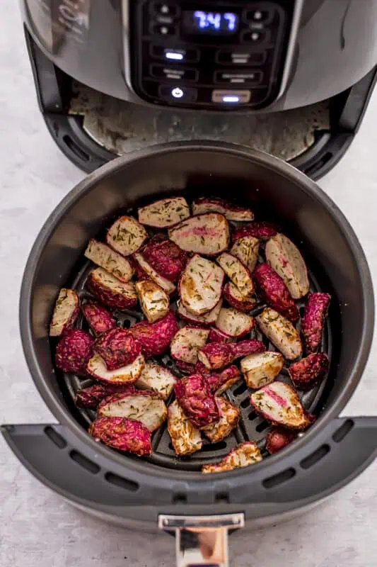 Radishes in air fryer basket cooking about half way before being shaken.