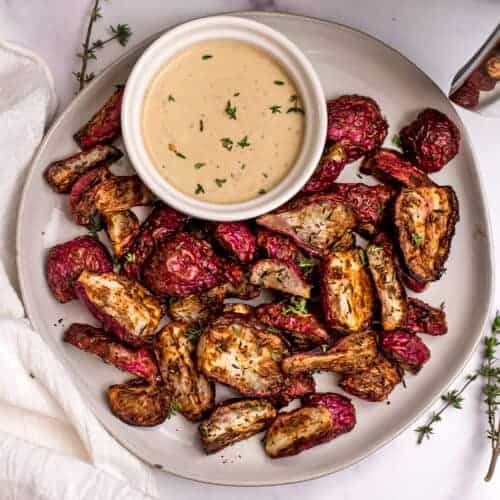 Air fryer radishes on a white plate with dip in a ramekin on the plate.