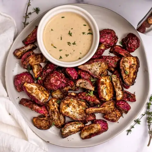 Air fryer radishes on a white plate with dip in a ramekin on the plate.