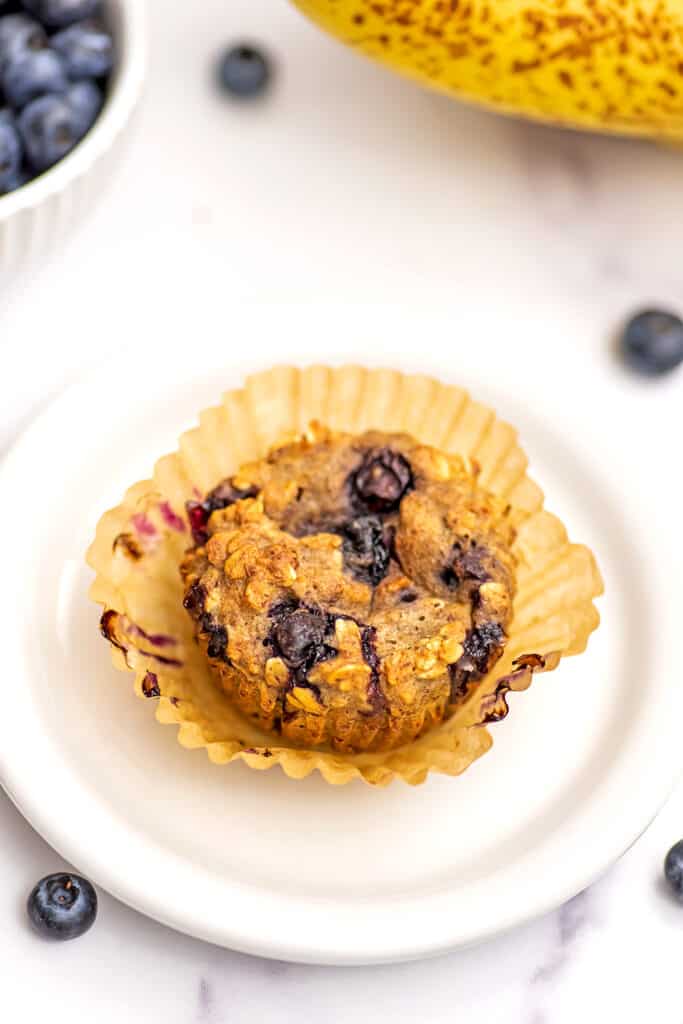 Blueberry banana oatmeal muffin on white plate with the parchment wrapper pulled off.
