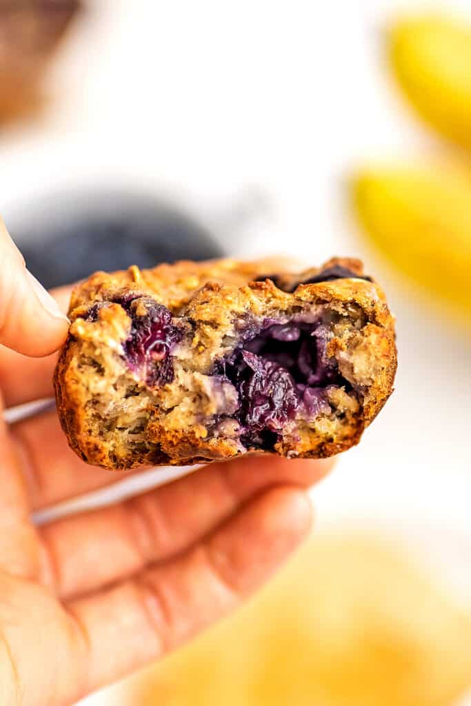 Hand holding blueberry banana oatmeal muffin that was cut in half.