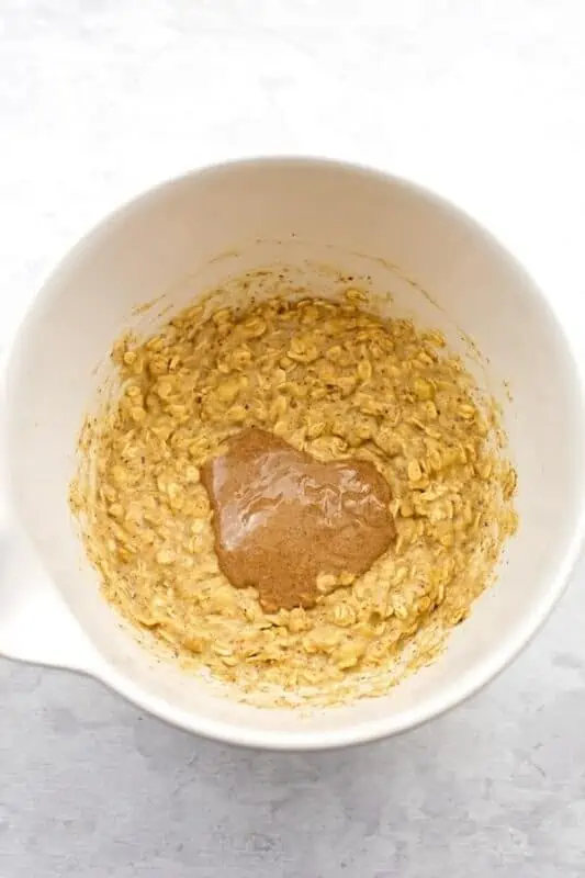 Almond butter added to oat muffin batter in white bowl.