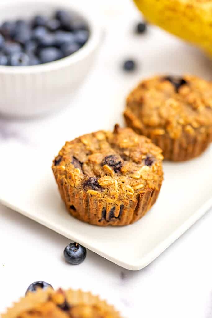 Blueberry banana oatmeal muffins on a white plate with blueberries in the background.