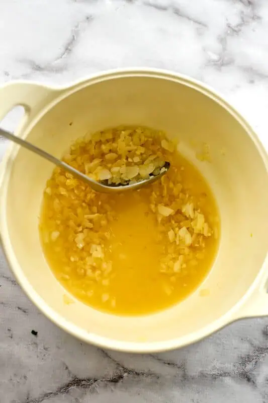 Spoon scraping the bottom of a pot with onions and vegetable broth in it.