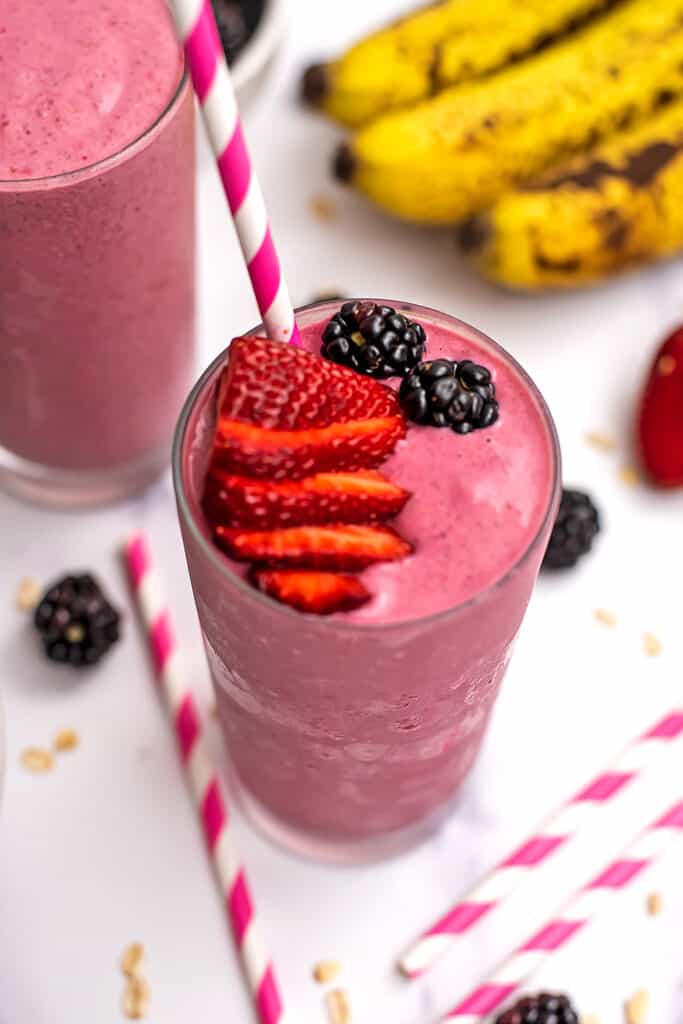 Strawberry blackberry banana smoothie in a glass with sliced strawberries and blackberry on top, straw in the glass.