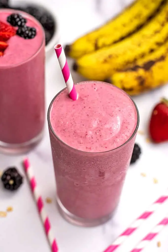 Pink striped straw in a glass of blackberry strawberry banana smoothie.