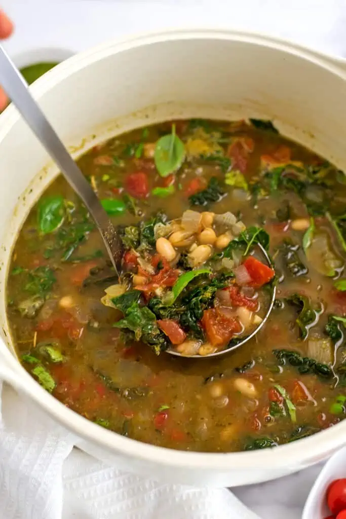 Silver ladle spooning out a serving of tuscan white bean soup with kale.