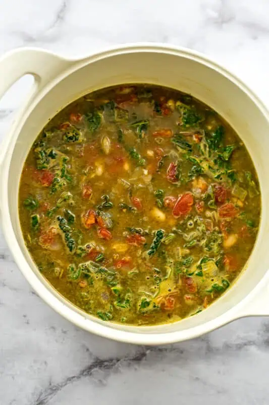 Italian white bean soup in white pot after adding kale.