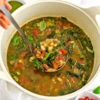 Ladle in pot of tuscan white bean soup with kale.