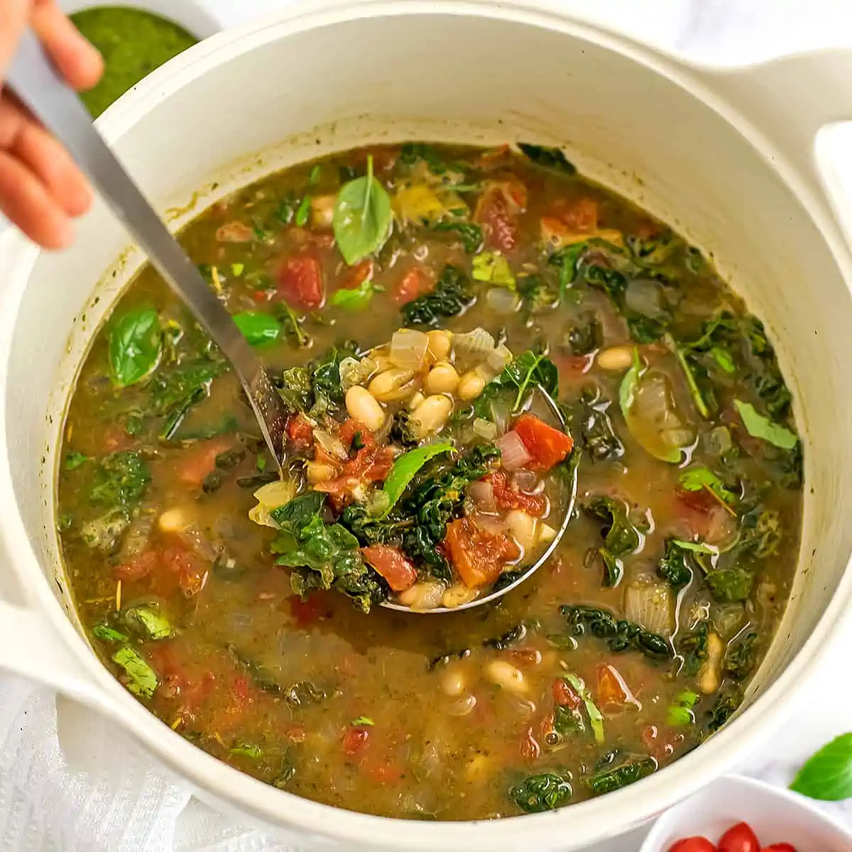Ladle in pot of tuscan white bean soup with kale.